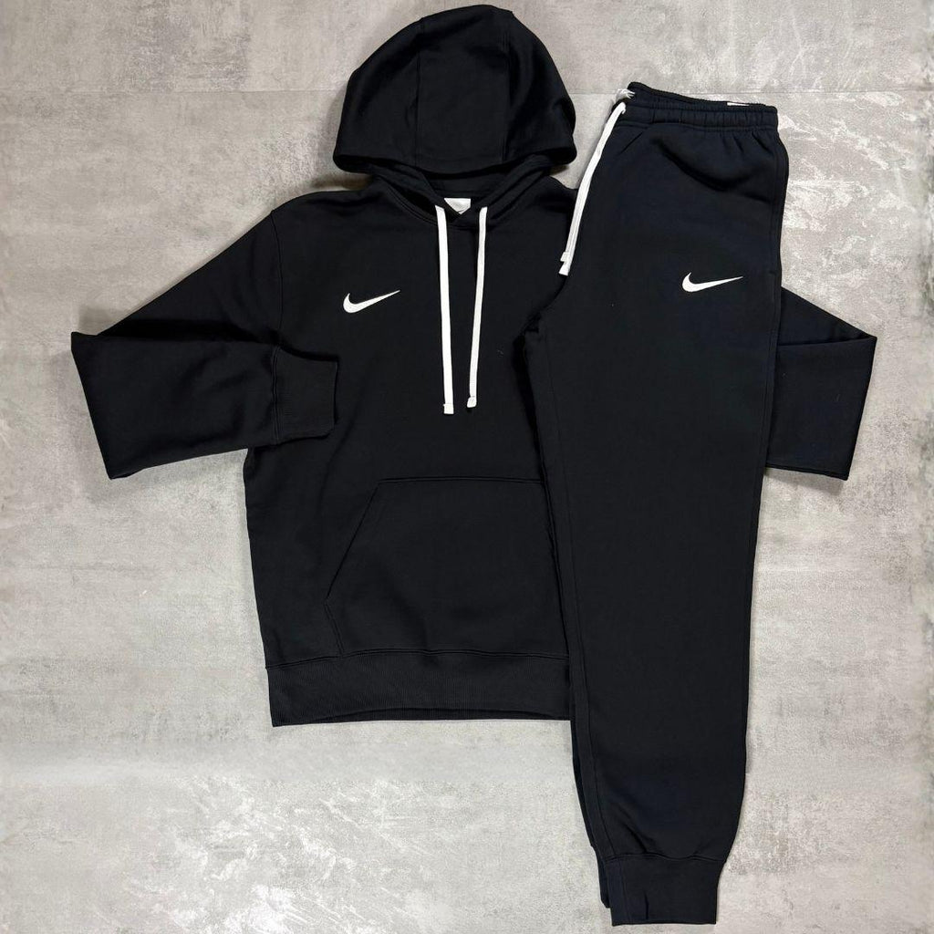 Nike Black Club Fleece Hoodie and Joggers Tracksuit for men, flat lay of black cotton fleece pullover hoodie with white drawcords and kangaroo pocket and matching cuffed joggers with white Nike swoosh