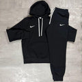 Nike Black Club Fleece Hoodie and Joggers Tracksuit for men, flat lay of black cotton fleece pullover hoodie with white drawcords and kangaroo pocket and matching cuffed joggers with white Nike swoosh