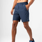 A man wearing navy blue Agaru Sports athletic shorts with side pockets and an elastic waistband, shown from the waist down against a light gray studio background.