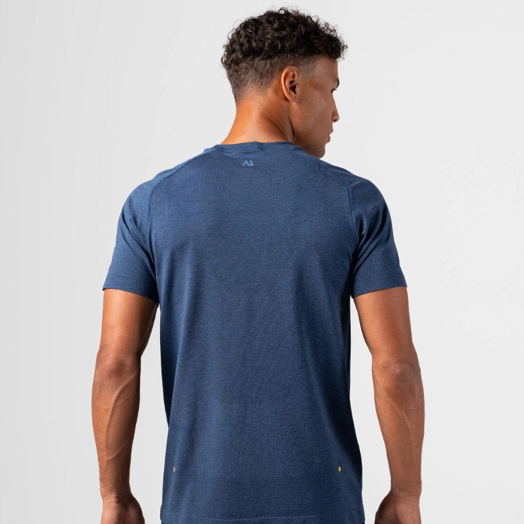 A man viewed from the back wearing a heathered blue short-sleeve athletic t-shirt, showing a small Agaru Sports logo on the upper back and subtle stitching details.