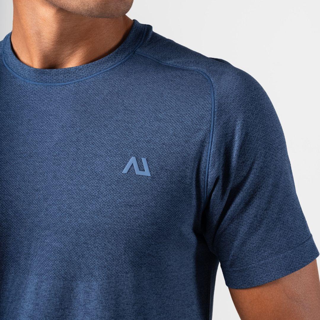Close-up of a man wearing a heathered blue short-sleeve athletic t-shirt with a light blue geometric Agaru Sports logo on the left chest, set against a plain light gray background.