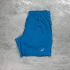 Asics Blue athletic shorts with a logo on a gray concrete surface