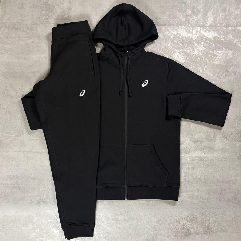 Asics Black Zip Up Hoodie and Jogger Tracksuit for men, flat lay of black full-zip hooded top with kangaroo pockets and ribbed cuffs and matching black joggers with white Asics logo