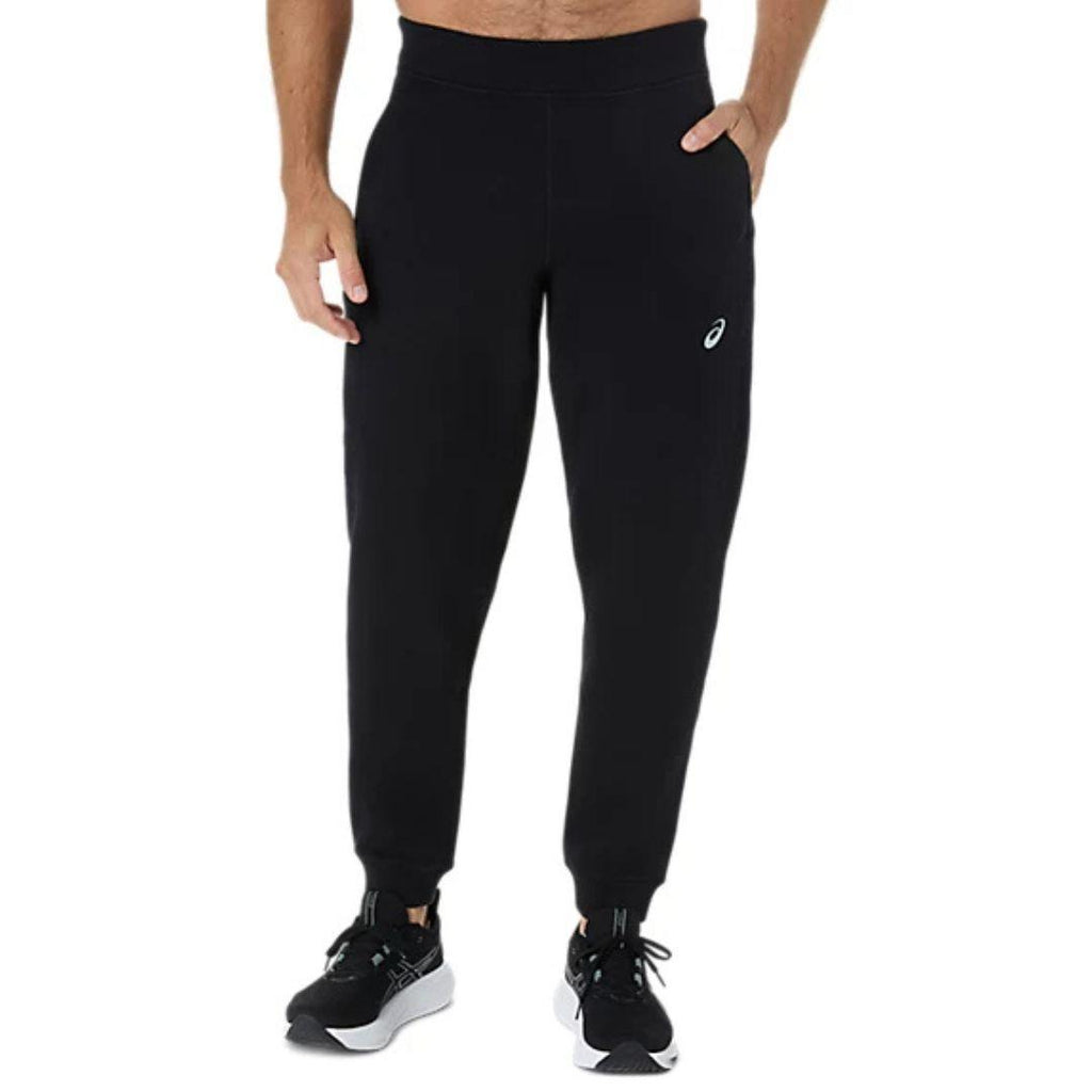 Asics Black Jogger for men, front view on model of black joggers with elasticated waistband, side pockets, ribbed ankle cuffs and white Asics logo on the thigh, part of the Asics Black Tracksuit