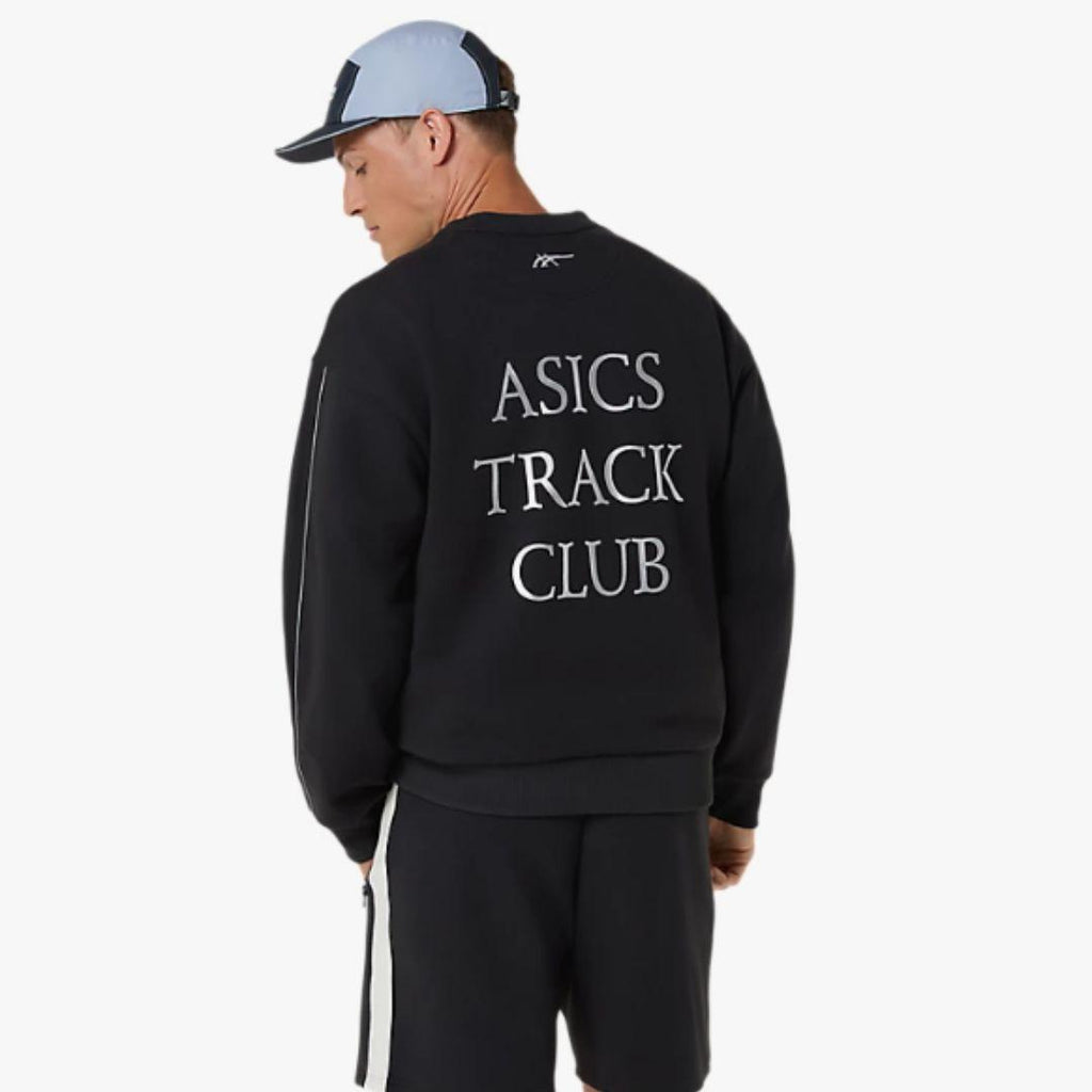 A man wearing a black Asics track sweatshirt from the back, featuring 'ASICS TRACK CLUB' printed in white text, paired with black track pants and a light blue and black baseball cap, against a plain white background.