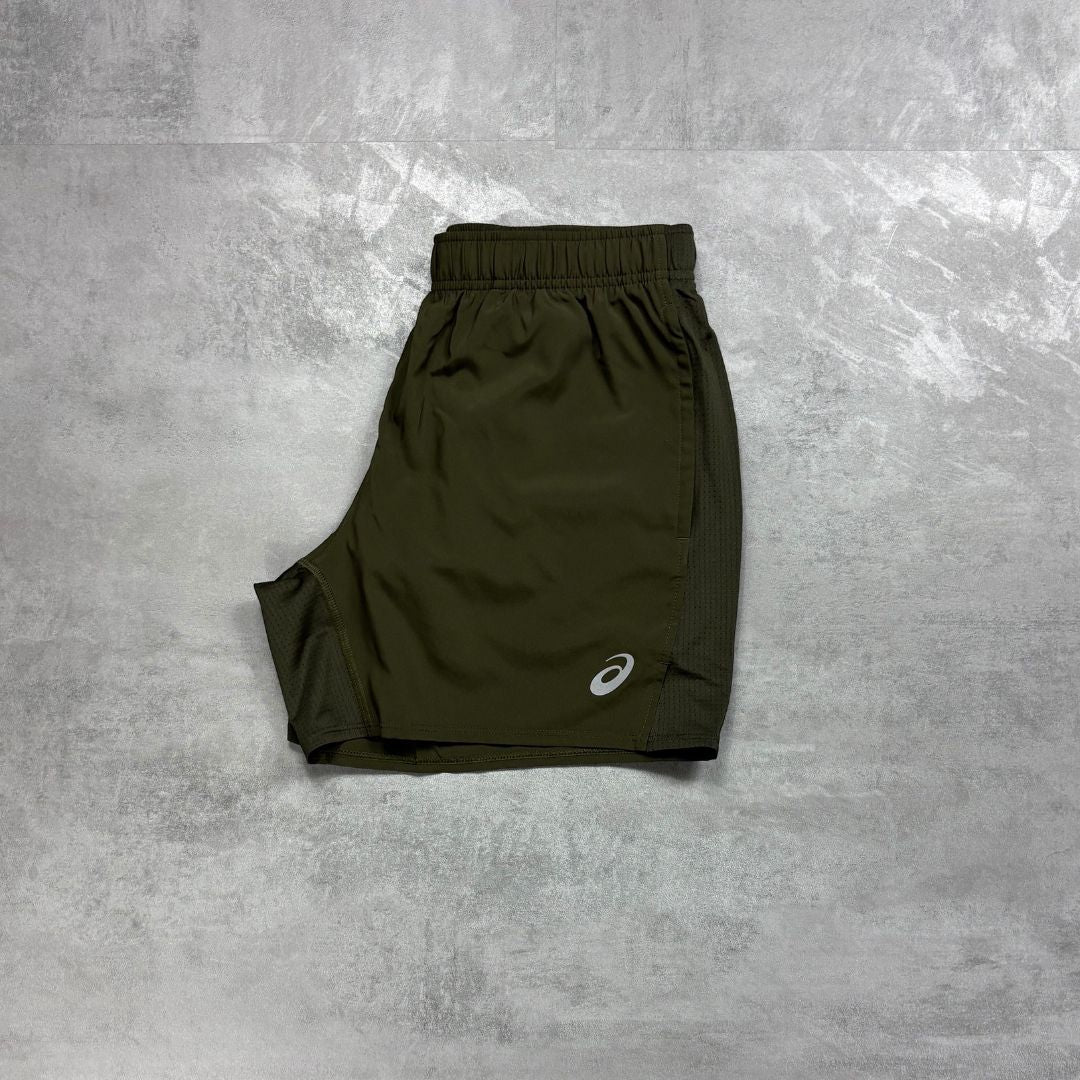Asics Brown Stone core shorts flat laid out on a grey concrete flooring