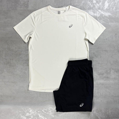 A white short-sleeve athletic t-shirt and black athletic shorts laid flat on a gray textured surface. Both garments feature a small white Asics logo on the chest and lower leg.