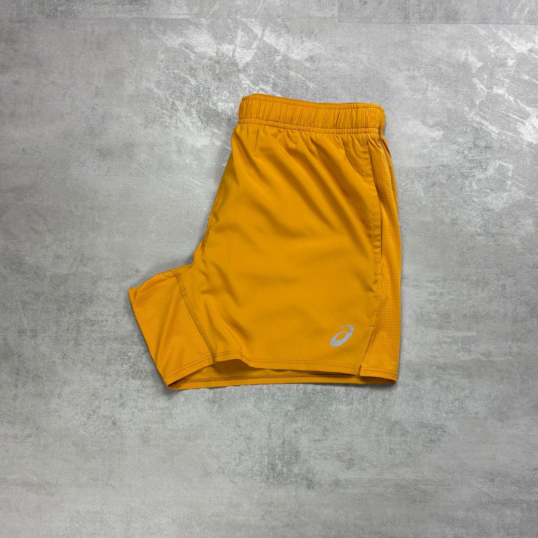 Asics orange shorts with a brand logo on a gray concrete surface