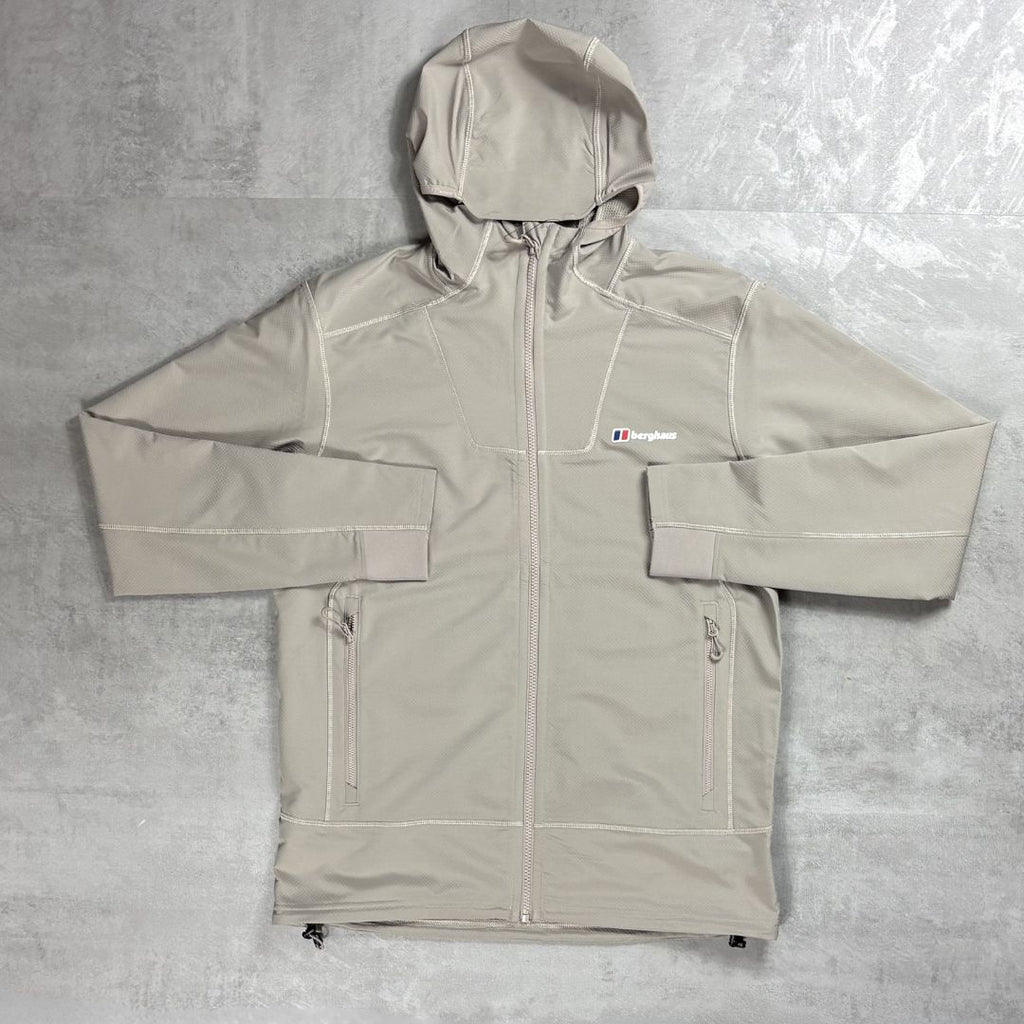 A light beige hooded jacket with white contrast stitching, laid flat on a textured gray background. A small embroidered logo on the left chest reads Berghaus.