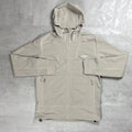 A light beige hooded jacket with white contrast stitching, laid flat on a textured gray background. A small embroidered logo on the left chest reads Berghaus.