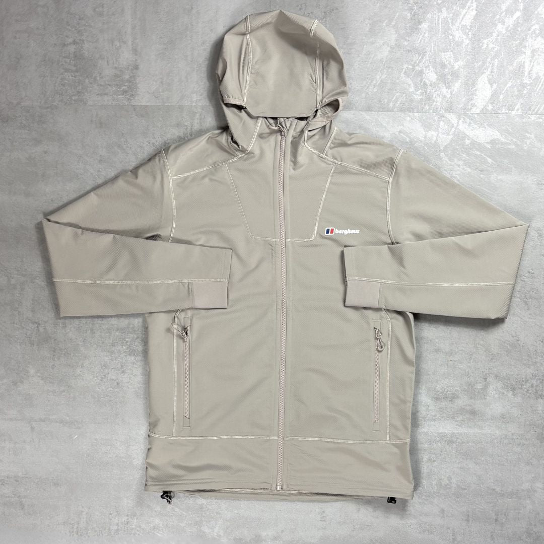 A light beige hooded jacket with white contrast stitching, laid flat on a textured gray background. A small embroidered logo on the left chest reads Berghaus.