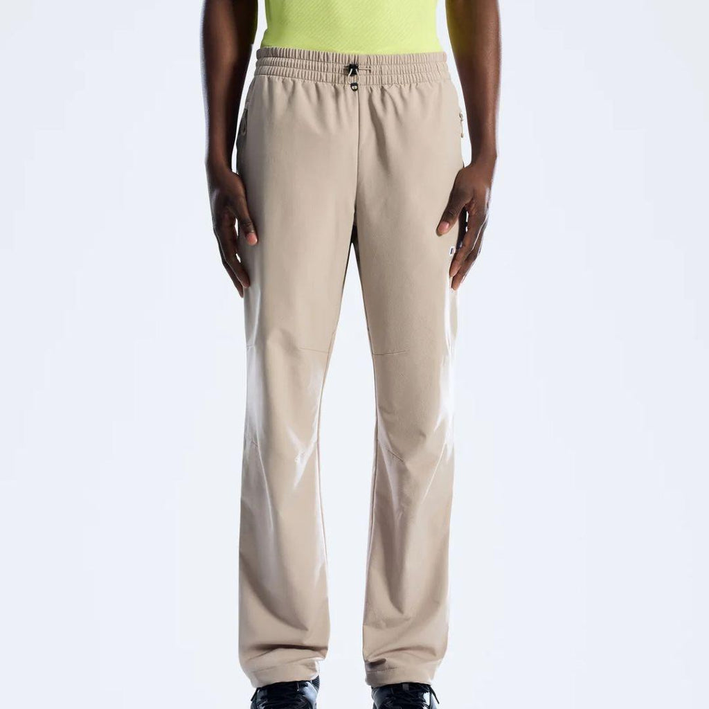 A person wearing beige Berghaus straight-leg sweatpants with an elastic waistband and drawstring, paired with a neon yellow top and black shoes, shown against a plain light gray studio background.