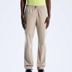 A person wearing beige Berghaus straight-leg sweatpants with an elastic waistband and drawstring, paired with a neon yellow top and black shoes, shown against a plain light gray studio background.