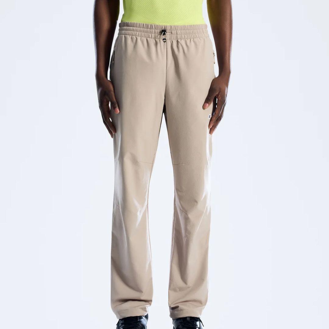 A person wearing beige Berghaus straight-leg sweatpants with an elastic waistband and drawstring, paired with a neon yellow top and black shoes, shown against a plain light gray studio background.