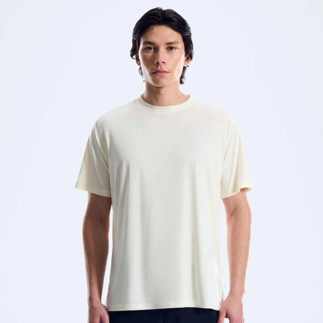 A man wearing a plain cream-colored short-sleeve crewneck t-shirt, standing against a light gray studio background.