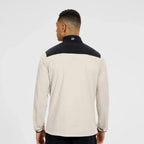 A man viewed from the back wearing a long-sleeve athletic jacket with a cream body and a black yoke across the shoulders, on a light gray studio background.