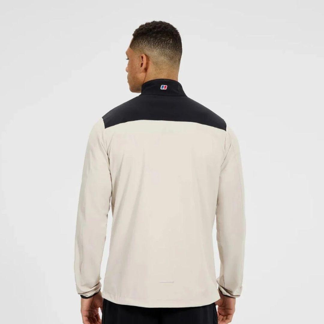 A man viewed from the back wearing a long-sleeve athletic jacket with a cream body and a black yoke across the shoulders, on a light gray studio background.