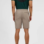 A man viewed from the back wearing beige cargo shorts and a dark green t-shirt, standing against a light gray studio background.