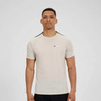 A man wearing a light beige athletic t-shirt with black shoulder panels and a small red and blue Berghaus logo on the chest, photographed against a light gray studio background.
