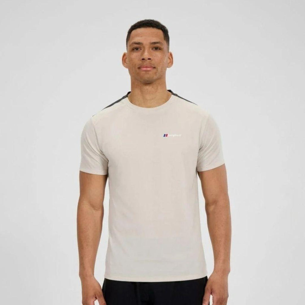 A man wearing a Berghaus light beige short-sleeve athletic t-shirt with black shoulder stripes and a small red and blue logo on the chest, photographed against a light gray studio background.
