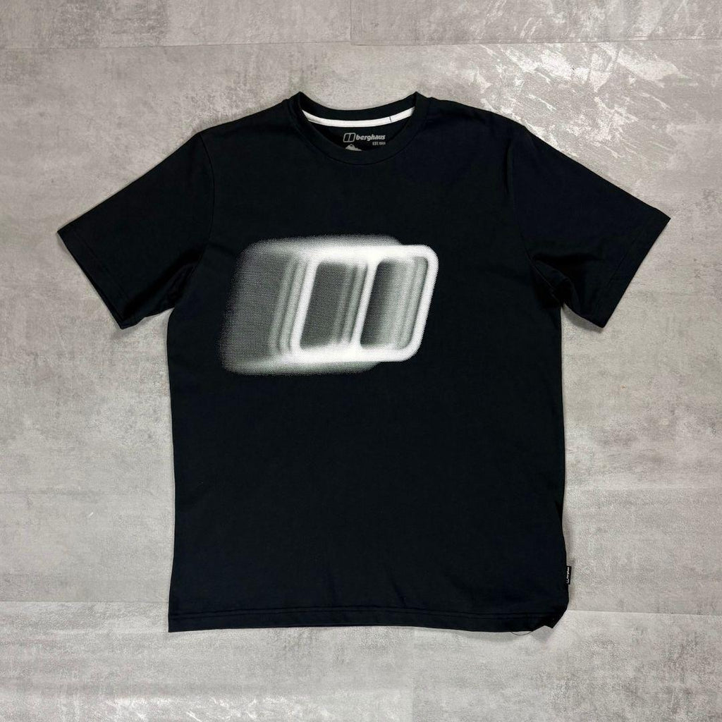 Berghaus Black Blockmorph Essential T-Shirt for men, flat lay on a grey concrete surface of the black crew neck tee with blurred Berghaus block logo graphic across the chest