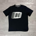 Berghaus Black Blockmorph Essential T-Shirt for men, flat lay on a grey concrete surface of the black crew neck tee with blurred Berghaus block logo graphic across the chest