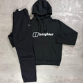 A black Berghaus hoodie and matching black jogger pants laid flat on a textured gray concrete surface. The hoodie features a white printed logo on the chest, and the joggers have an elastic waist and a small white logo on the left pocket.