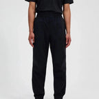 A person wearing loose black Berghaus jogger-style pants with an elastic waistband and side pockets, shown from the chest down against a plain light gray studio background.