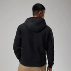 A man viewed from behind wearing a black pullover hoodie and tan pants against a plain light gray studio background.
