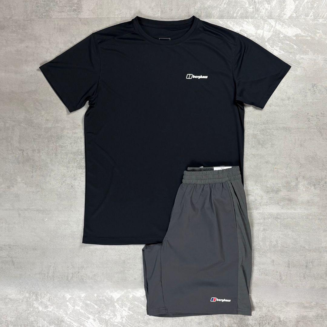 A two-piece athletic set from Berghaus, featuring a black short-sleeve performance t-shirt and dark gray shorts, laid flat on a textured gray concrete surface.