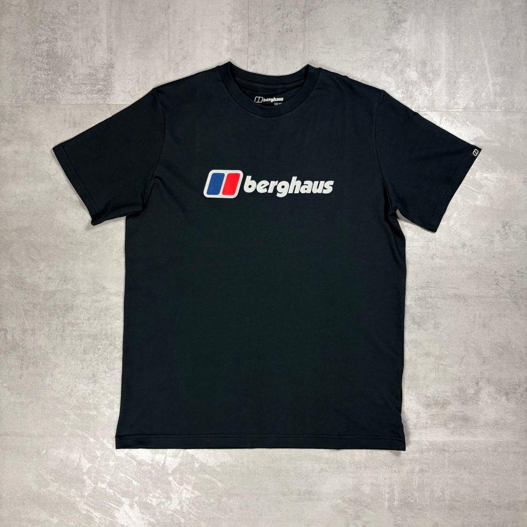 A black short-sleeve crewneck t-shirt featuring the Berghaus logo printed on the chest, laid flat on a textured gray concrete surface.