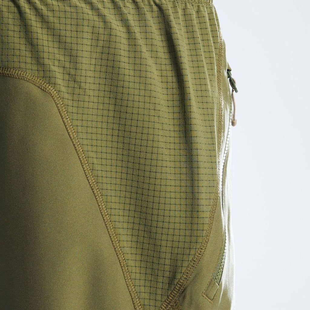 Close-up of olive green athletic shorts showing a fine grid pattern on the upper section, solid fabric on the lower section, and a side zipper.
