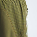 Close-up of olive green athletic shorts showing a fine grid pattern on the upper section, solid fabric on the lower section, and a side zipper.