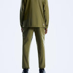 A model shown from the back wearing an olive green athletic tracksuit, featuring a long-sleeve top and matching pants, against a light gray studio background.