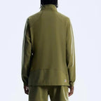 A person shown from the back wearing an olive green athletic jacket and matching pants against a clean light gray studio background.