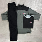 A flat lay of a three-piece Berghaus outdoor clothing set on a textured gray concrete background. The set includes a black and gray quarter-zip pullover, matching black trousers, and a black short-sleeve T-shirt with a small Berghaus logo on the chest.