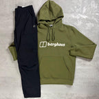 An olive green hoodie and black pants set from the brand Berghaus, laid flat on a textured gray concrete background. The hoodie features the white 'berghaus' logo across the chest.