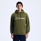A man wearing an olive green pullover hoodie with a white printed 'berghaus' logo on the chest, paired with dark pants, photographed against a clean white studio background.