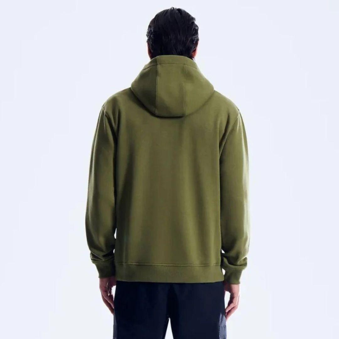 A man viewed from the back wearing an olive green pullover hoodie and dark pants against a plain light gray studio background.