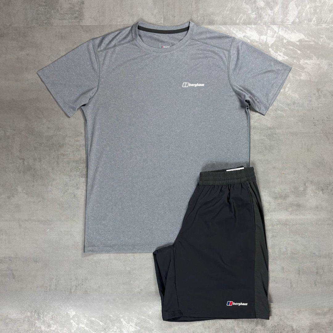 A gray short-sleeve athletic t-shirt and black athletic shorts from the brand Berghaus, laid flat on a gray textured concrete surface.