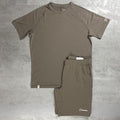 A two-piece athletic set consisting of a Berghaus short-sleeve t-shirt and matching shorts in a muted taupe-brown color, laid flat on a gray textured surface. The brand name Berghaus is visible on the lower hem of the shirt and on the lower left leg of the shorts.