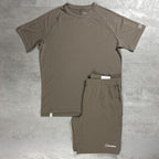 A two-piece athletic set consisting of a Berghaus short-sleeve t-shirt and matching shorts in a muted taupe-brown color, laid flat on a gray textured surface. The brand name Berghaus is visible on the lower hem of the shirt and on the lower left leg of the shorts.