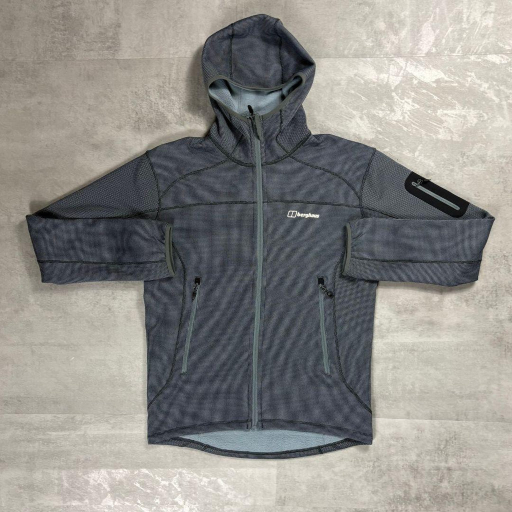 A dark gray hooded technical jacket with a subtle grid pattern, laid flat on a textured gray surface. The jacket features a full-length front zipper, two zippered hand pockets, a reflective arm patch on the upper sleeve, and a white Berghaus logo on the left chest.