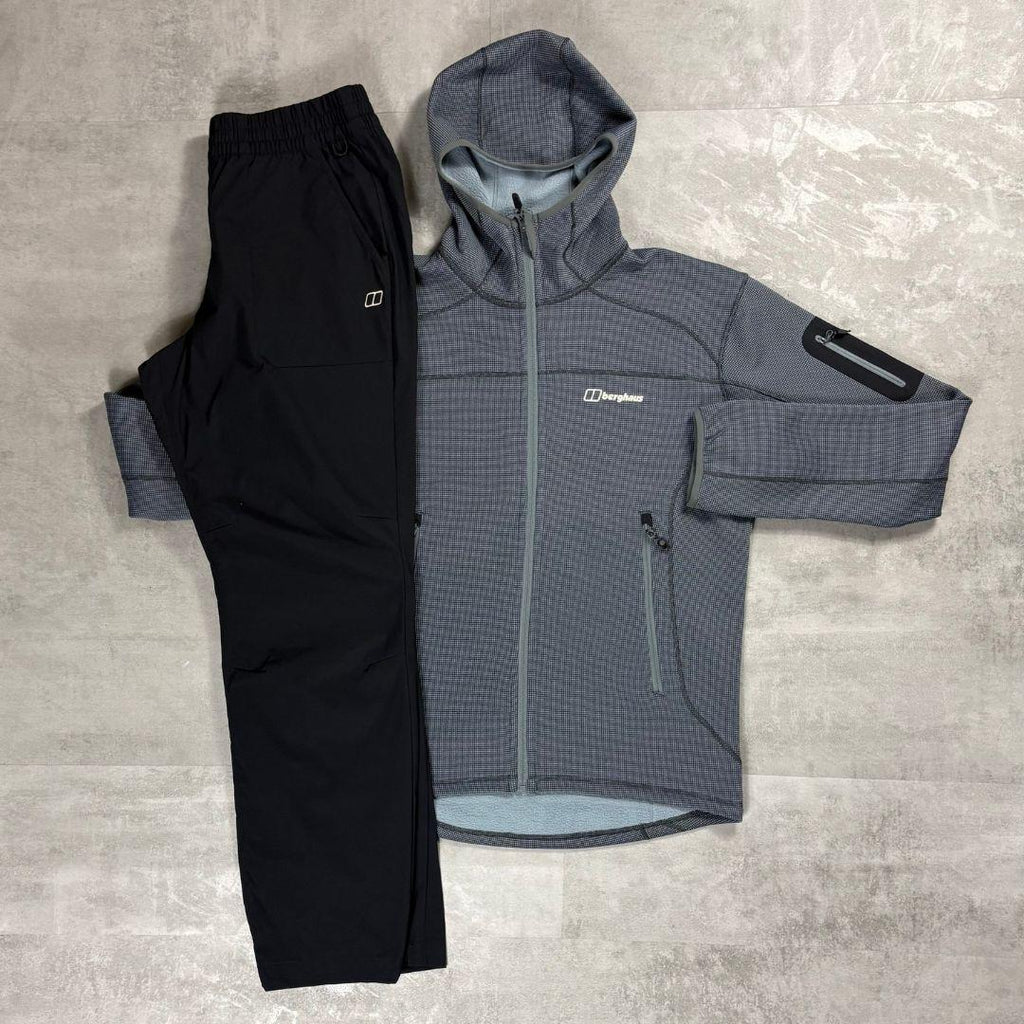 A flat-lay view of a two-piece outdoor apparel set consisting of a gray and black patterned hooded jacket and black pants, laid out on a gray textured floor. The brand name Berghaus is visible on the chest of the jacket.