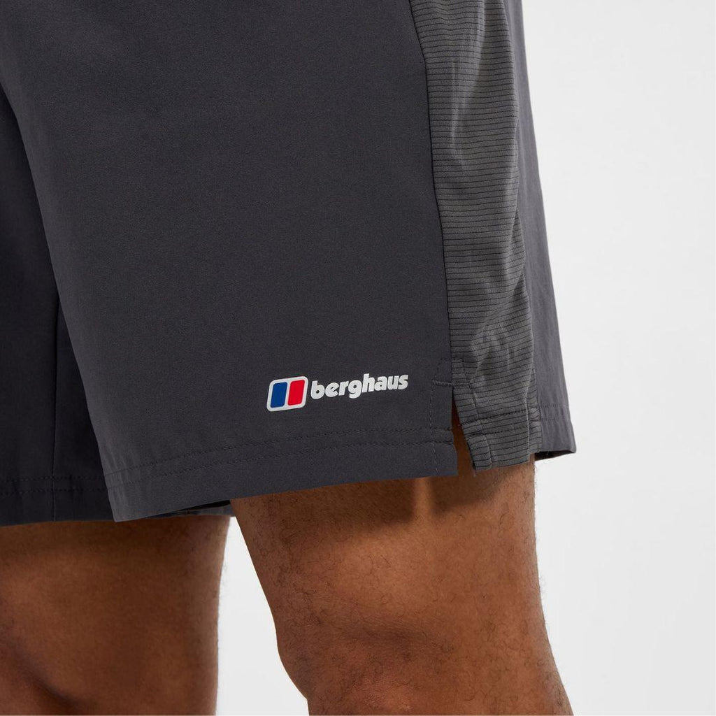Close-up of a person wearing dark charcoal gray Berghaus athletic shorts, showing the side logo and the model's legs against a light gray background.