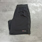 A pair of dark gray athletic shorts with an elastic waistband and a small Berghaus logo on the lower left leg, laid flat on a textured gray concrete surface.