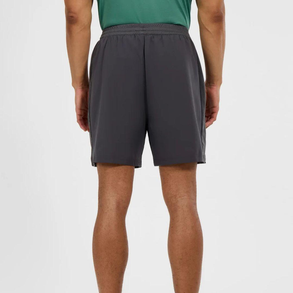 A person shown from the back wearing dark gray athletic shorts and a green top, photographed against a clean light gray studio background.