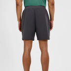 A person shown from the back wearing dark gray athletic shorts and a green top, photographed against a clean light gray studio background.