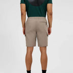 A man viewed from the back wearing beige cargo shorts and a dark green t-shirt, standing against a light gray studio background.