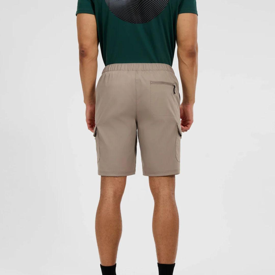 A man viewed from the back wearing beige cargo shorts and a dark green t-shirt, standing against a light gray studio background.